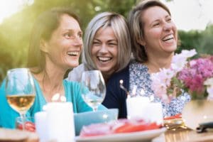 three female friends in their 40s share a moment of complicity. They gathered around a table in the garden to share a meal with friends.